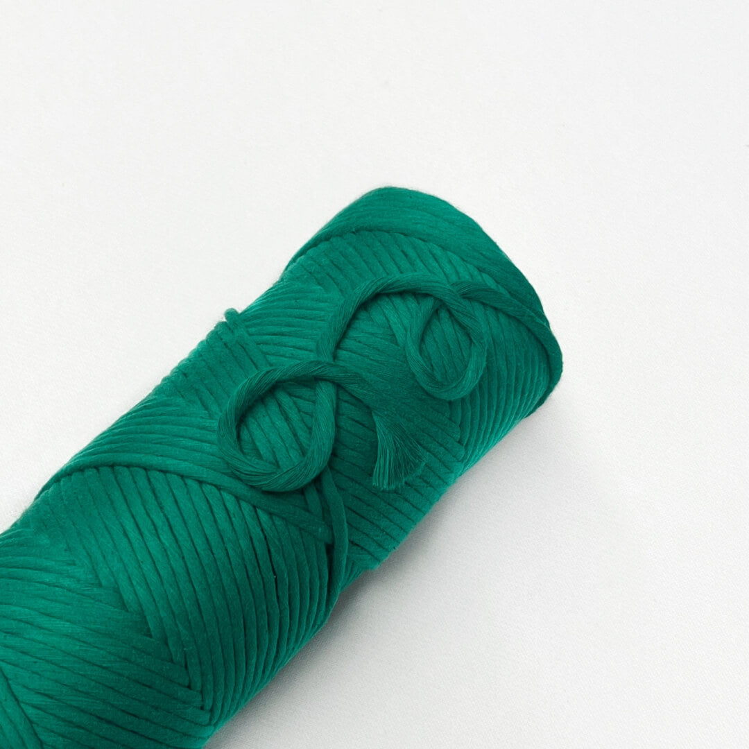 single roll of deep jewel green macrame cord laying flat on white wall