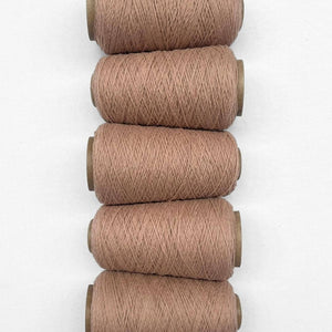 Five cones of muted peach wool cord laying flat vans vertical on whtie background