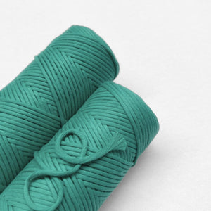 two rolls of sea green macrame cord laying flat on white wall